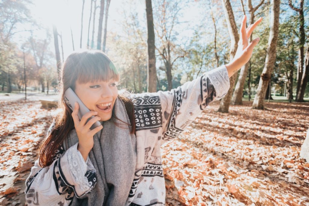 Young woman having a fun call during a sunset at the forest during an autumnal winter day. Connectivity and social concept.Young people life style. Greeting friends online. Copy space.